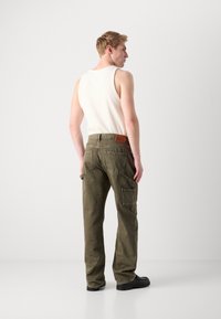 Olive green cargo pants with multiple pockets, textured fabric, and a brown leather patch at the waist. Slim fit design.
