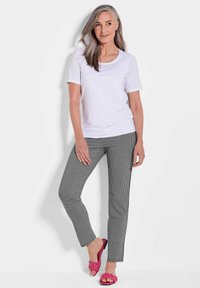 Weißes T-Shirt mit kurzen Ärmeln, gemusterte schwarz-weiße Karohose und rosa geflochtene Sandalen. Glatter Stoff mit lockerer Passform.