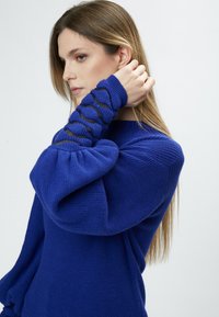 Strickpullover in lebhaftem Blau mit strukturierten, gepufften Ärmeln und Ausschnitten an den Bündchen, mit einer weichen und glatten Oberfläche.