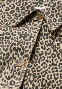 Tessuto con stampa leopardata caratterizzato da uno sfondo beige con macchie nere, cuciture dettagliate e un bottone metallico rotondo.