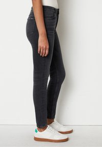 Slim-fit mustat farkut sisältävät klassisen viiden taskun muotoilun, hienovaraisen haalistumisen ja keskipitkän vyötärön. Asusteena ovat valkoiset tennarit.