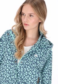 Chaqueta con estampado de leopardo en color verde azulado, confeccionada con material ligero. Presenta una capucha, cierre de cremallera y dos bolsillos frontales con broche. Detalle sutil del logo.