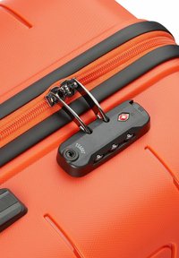 Valigia rigida arancione con superficie texturizzata, zip nera e lucchetto TSA. Presenta un design robusto con accenti neri a contrasto.