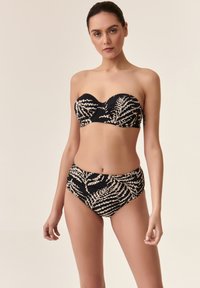 Bikini de patrón negro y crema, con un top sin tirantes con fruncidos y braguitas de cintura alta, textura suave y motivos de hojas.