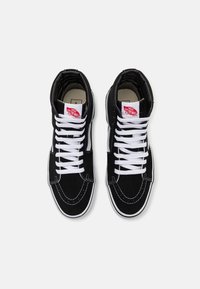 Baskets montantes noires avec lacets blancs, tige en suède et toile, col rembourré, marque Vans sur la languette et détails de couture contrastants.