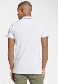 Grå polo-shirt med en klassisk krave, prydet med kontrasterende marineblå striber på ærmerne. Materialet virker blødt og har en afslappet pasform.
