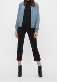 Lyseblå bomberjakke, sort ribbet top, sorte cropped jeans og sorte ankelstøvler. Glat stof, lynlåslukning foran og tætsiddende design.