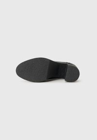 Chaussure en cuir noir avec un dessus lisse, un embout arrondi et une semelle en caoutchouc texturée. Présente un talon bas et effilé pour plus de stabilité.