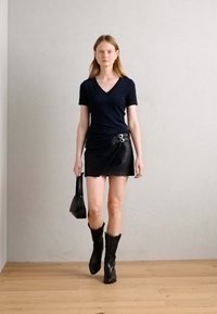 T-shirt bleu marine à col en V associé à une jupe-culotte en cuir noir ornée de quincaillerie argentée, des bottes noires hauteur genou et un petit sac à main noir.