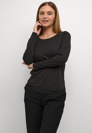 Must musta varrukatega särk pehmest kangast, ümar kaelus ja kitsas lõige, koos mustade pükstega. Lihtne, sile tekstuur.
