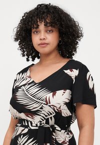 Black dress with short sleeves, featuring a v-neckline and a pattern of white and brown tropical leaves. Tied belt at the waist.