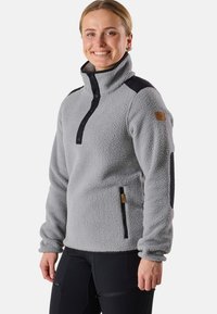 Grå fleece-tröja med svarta detaljer, hög krage, dragkedja på sidfickan och textilier med struktur, med knäppning framtill och logotypmärke.