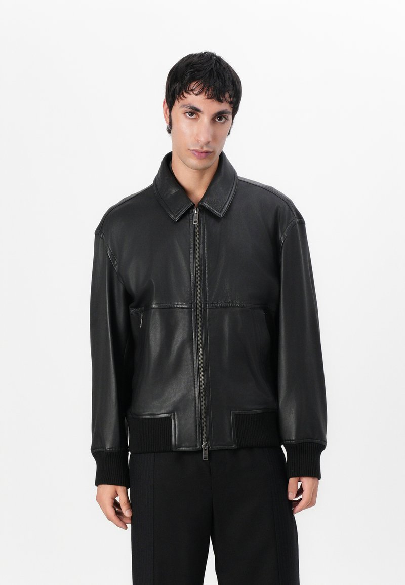 Black leather jacket with a zip front, wide collar, ribbed cuffs, and a smooth texture. Features front pockets and a relaxed fit design.
