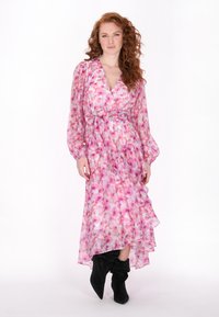 Lang roze bloemen wikkeljurk met een vloeiende, gerimpelde zoom en doorzichtige stof. Combinatie met zwarte, tot de knie reikelende, spitse laarzen.