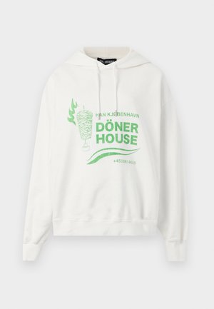 Baltas džemperis ar zaļu grafiku, kurā attēlots döner kebaba gaļas gabals uz grila šķēles, liesmas un uzraksts "Döner House" ar tālruņa numuru priekšpusē.