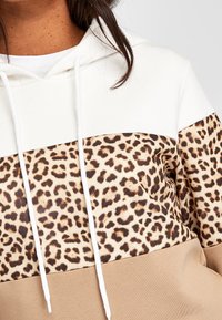 Sudadera con capucha que presenta un panel superior blanco, una sección media con estampado de leopardo y un panel inferior beige. Fabricada en tela suave con cordones.