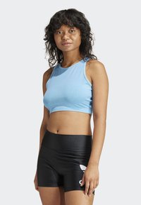 Gaiši zils cropped sporta tops ar apaļu kakla izgriezumu, apvienots ar melnām spīdīgām šortiem ar baltu logo, piemērots sportiskām aktivitātēm.
