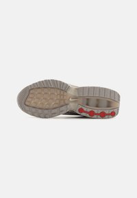 Nike sneaker outsole in beige and grey with textured rubber. Features red circular accents and a visible air cushioning unit.