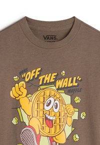 Braunes Baumwoll-T-Shirt mit einem Cartoon-Waffel-Charakter, lebendigen Farben, runder Form und dem Text "OFF THE WALL" in fettem Schwarz und Gelb.