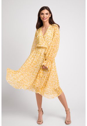 Żółta sukienka w obiegu z białym abstrakcyjnym wzorem, długimi rękawami i paskiem do przewiązania w talii. Przewiewny materiał i długość do połowy łydki.