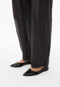 Černé kožené baleríny se špičatou špičkou a nízkým profilem, kombinované s volnými černými koženými kalhotami s knoflíkovým detailem na lemu.