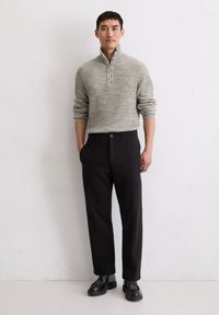 Hellgrauer, gestrickter Halbzip-Pullover, schwarze, maßgeschneiderte Hose und schwarze Schnürschuhe. Glatte Textur mit einem gerippten Muster auf dem Pullover.