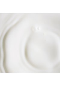 Un liquide blanc avec une texture lisse et fluide, présentant de petites bulles et ondulations. La surface paraît brillante et réfléchissante.