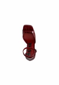 Escarpin en cuir verni rouge avec un bout carré, une sangle de cheville et un design découpé. La semelle intérieure présente des lettres noires. Fini lisse et brillant.