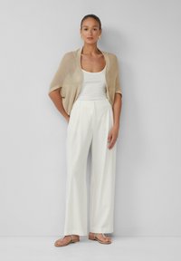 Beige gebreide cardigan met korte mouwen over een witte tanktop, gecombineerd met brede witte broek en zilveren sandaaltjes met bandjes. Glad textuur.