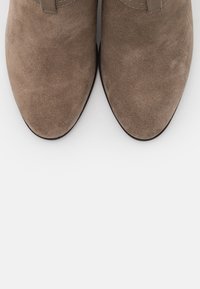 Stivaletti alla caviglia in suede marrone con punta affusolata, caratterizzati da una superficie liscia e un design minimalista. Nessun hardware o motivo visibile.
