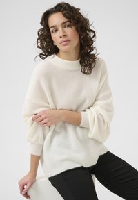 Pulover alb, pufoș cu tricotaj, cu guler rotund, umeri lăsați și manșete cu talie. Purtați-l peste pantaloni negri. Textură moale, cu o croială lejeră.