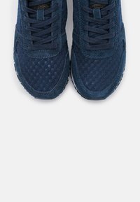 Baskets bleu marine en mesh et suède avec des surfaces texturées, dotées de lacets plats, d'une pointe ronde et de semelles en caoutchouc blanc.