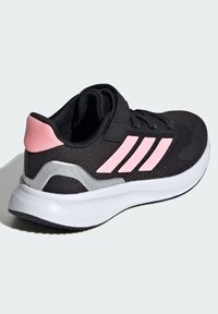 Black athletic shoe with a textured fabric upper, pink accents and three stripes, secured with a Velcro strap, featuring a white sole.