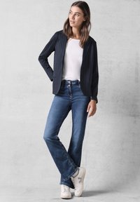 Blazer a righe navy sopra una maglietta bianca, abbinato a jeans chiari svasati e sneakers bianche. Tessuto morbido, vestibilità su misura, look casual.