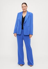 Blazer ajusté bleu et pantalon large assorti, en tissu lisse, avec un bouton unique, des revers en liséré et une coupe décontractée.