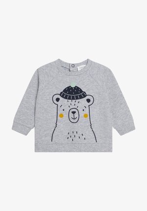 Lysegrå langærmet babytrøje med en enkel sort bamseansigt iført en mørkeblå strikhue med en grøn pompon og gule kinder.