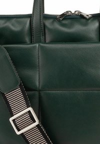 Groene leren tas met een gequiltde textuur, ritsluiting en een verstelbare gestreepte schouderband met een zilveren gesp. Heeft een minimalistisch ontwerp.