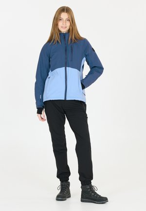 Veste bleu et bleu clair avec une fermeture éclair sur le devant, pantalon noir avec des poignets élastiques, et bottes de randonnée noires avec œillets en métal et lacets.