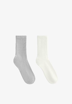 Pár ponožek v světle šedé a bílé barvě. Žebrovaná textury, délka po střed lýtek, měkká tkanina, jednoduchý design bez vzorů nebo doplňků.