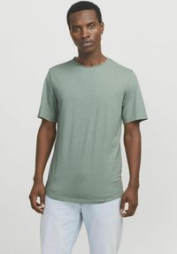 Green short-sleeve t-shirt made of soft fabric, featuring a classic crew neckline and a relaxed fit. Worn with light blue jeans.