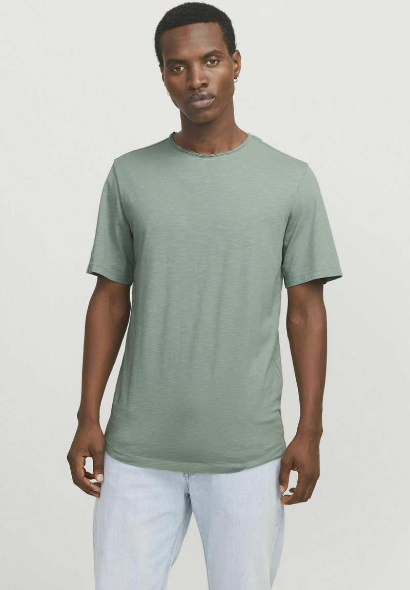 Green short-sleeve t-shirt made of soft fabric, featuring a classic crew neckline and a relaxed fit. Worn with light blue jeans.