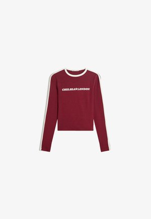 Burgundy long-sleeve top with white ribbed neckline and side stripes, featuring "CHELSEA★LONDON" printed on the front. Cotton material, cropped design.