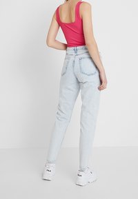 Sopiva vaaleanpunainen ribattupaita ja vaaleansiniset korkeavyötäröiset farkut; malli, joka pukeutuu valkoisiin lenkkareihin, esittelee rentoa asua selkäpuolelta.