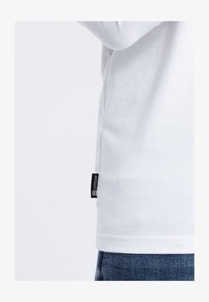 Bílé tričko s dlouhými rukávy a hladkým povrchem, na levé straně poblíž lemu je černý štítek značky "ombre". Viditelné zpevněné švy.