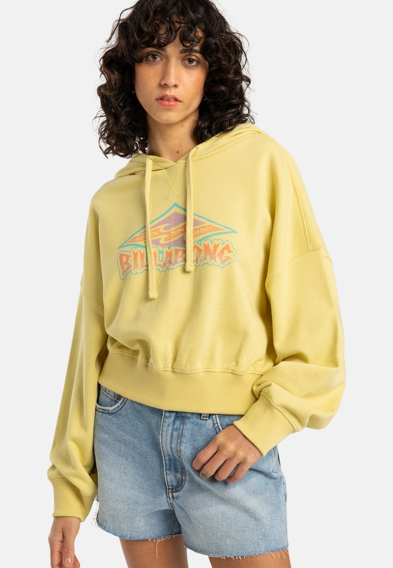 Yellow oversized hoodie with a graphic print, featuring a kangaroo pocket and ribbed hem. Paired with light blue denim shorts.