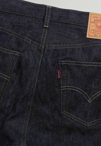 Vaqueros de mezclilla azul oscura de Levi's con costuras amarillas, que cuentan con una etiqueta de cuero y dos bolsillos traseros. Superficie texturizada con un ligero desvanecimiento.