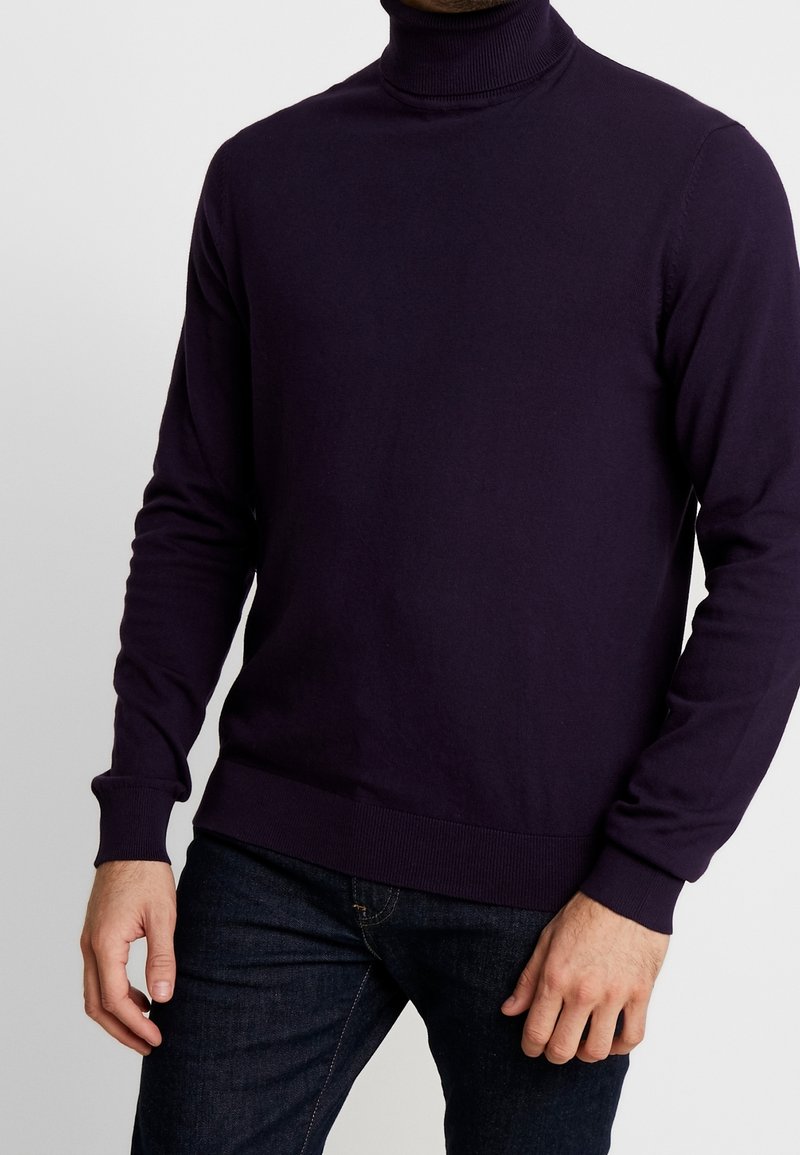 Pull à col roulé violet avec des manches longues, col et poignets côtelés. Texture lisse, coupe ajustée, associé à un jean sombre.