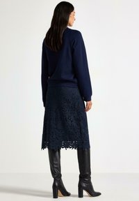 Marineblå sweatshirt med lange ærmer, parret med en knælang marineblå blondekjole med blomstermønster og sorte knæhøje støvler.