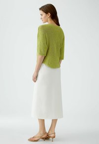 Green knitted sweater with elbow-length sleeves, paired with a white, flowy, midi skirt and tan heeled sandals. Smooth textures, relaxed fit.