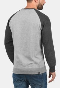 Felpa grigia con maniche raglan grigio scuro e polsini a costine, caratterizzata da un collo rotondo e un piccolo etichetta con logo sull'orlo.